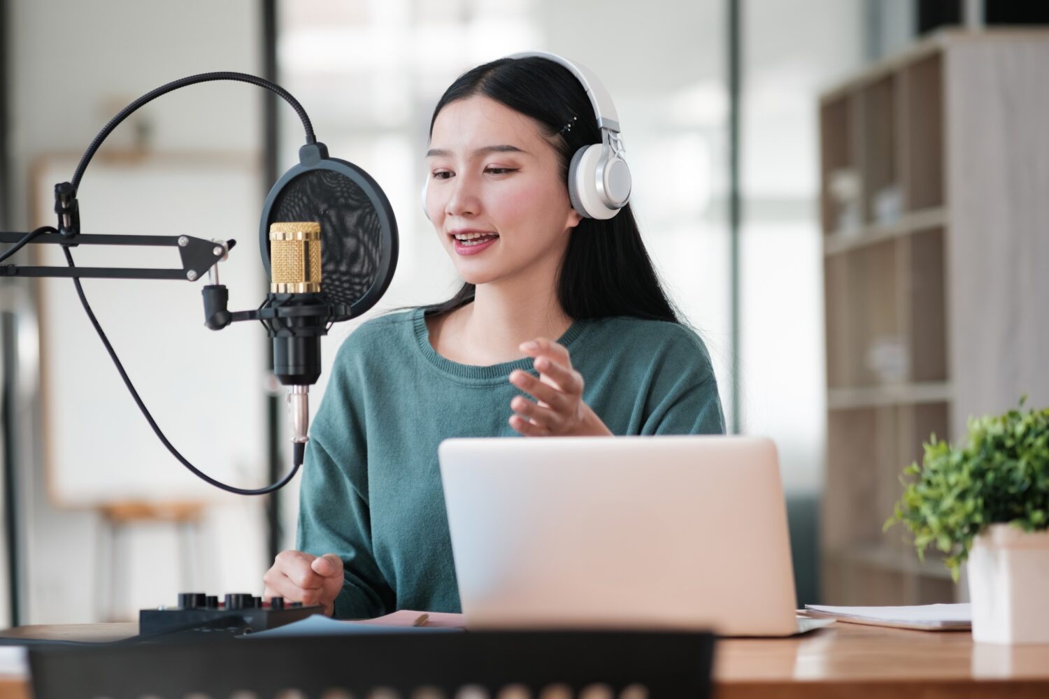 a-woman-is-sitting-at-a-desk-with-a-laptop-and-a-microphone-e1754464989196.jpg